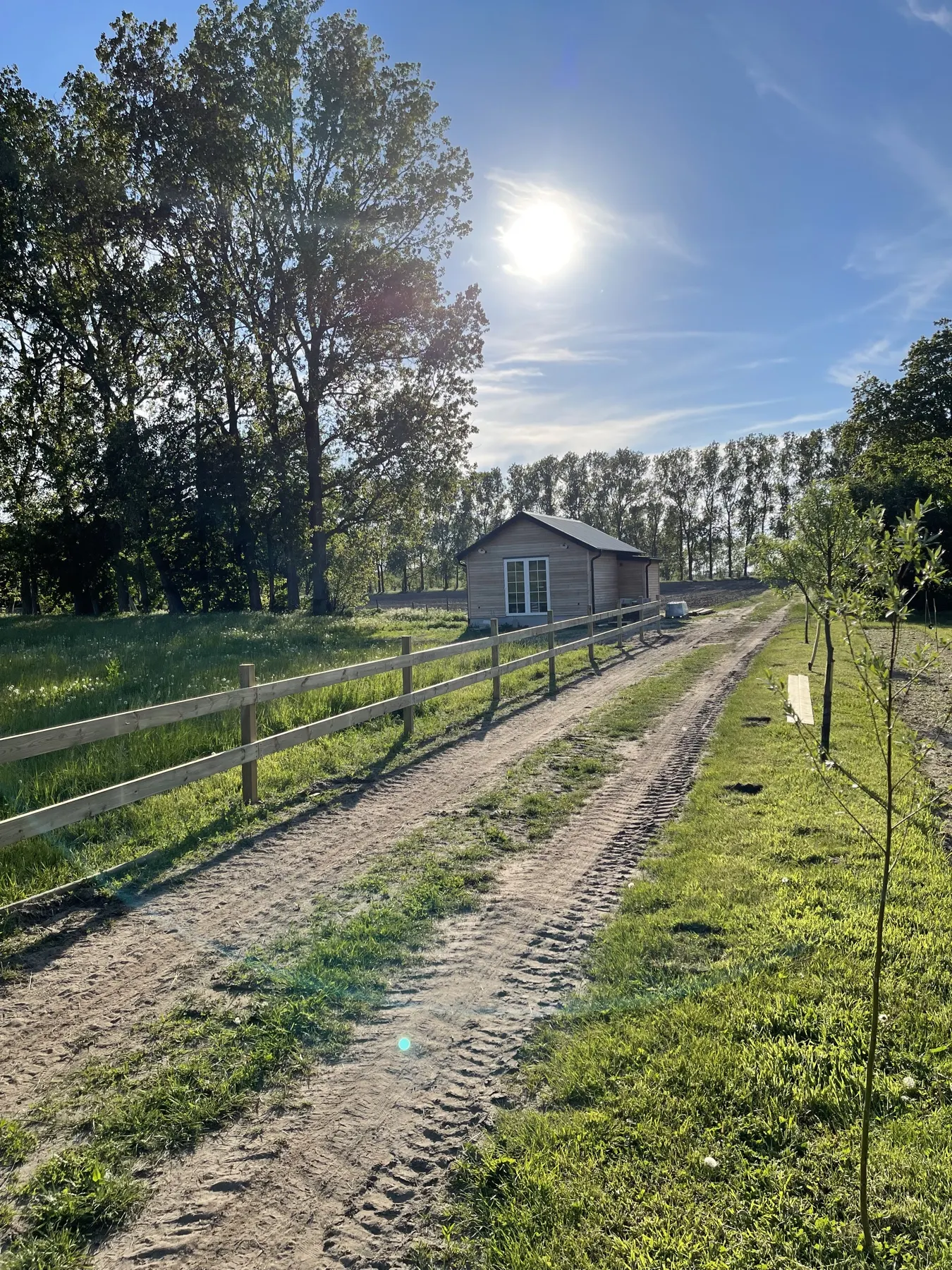 En grusväg längs ett trästaket mot ett litet trähus i motljus