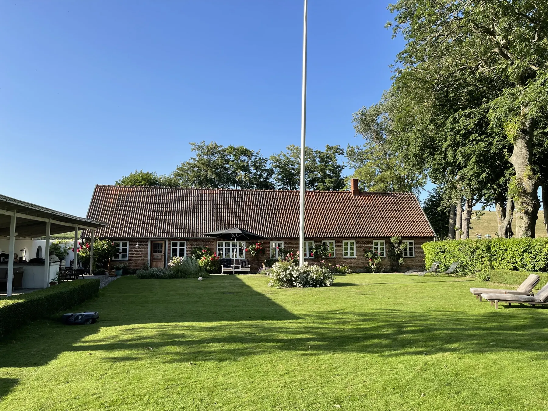 Tegelhuset med flaggstång och stor gräsmatta en solig sommardag