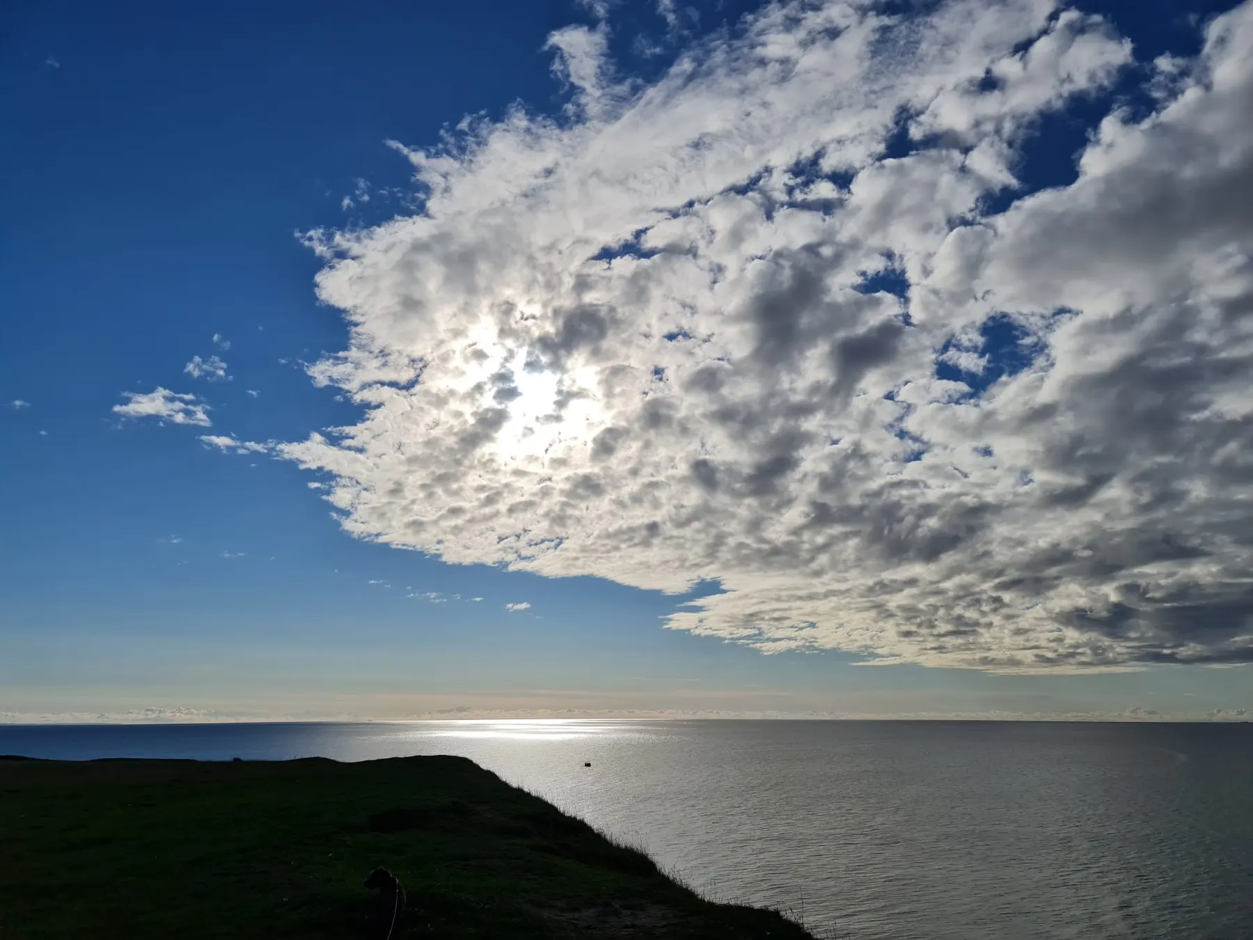Ett stort moln framför solen över havet, sett från en kulle