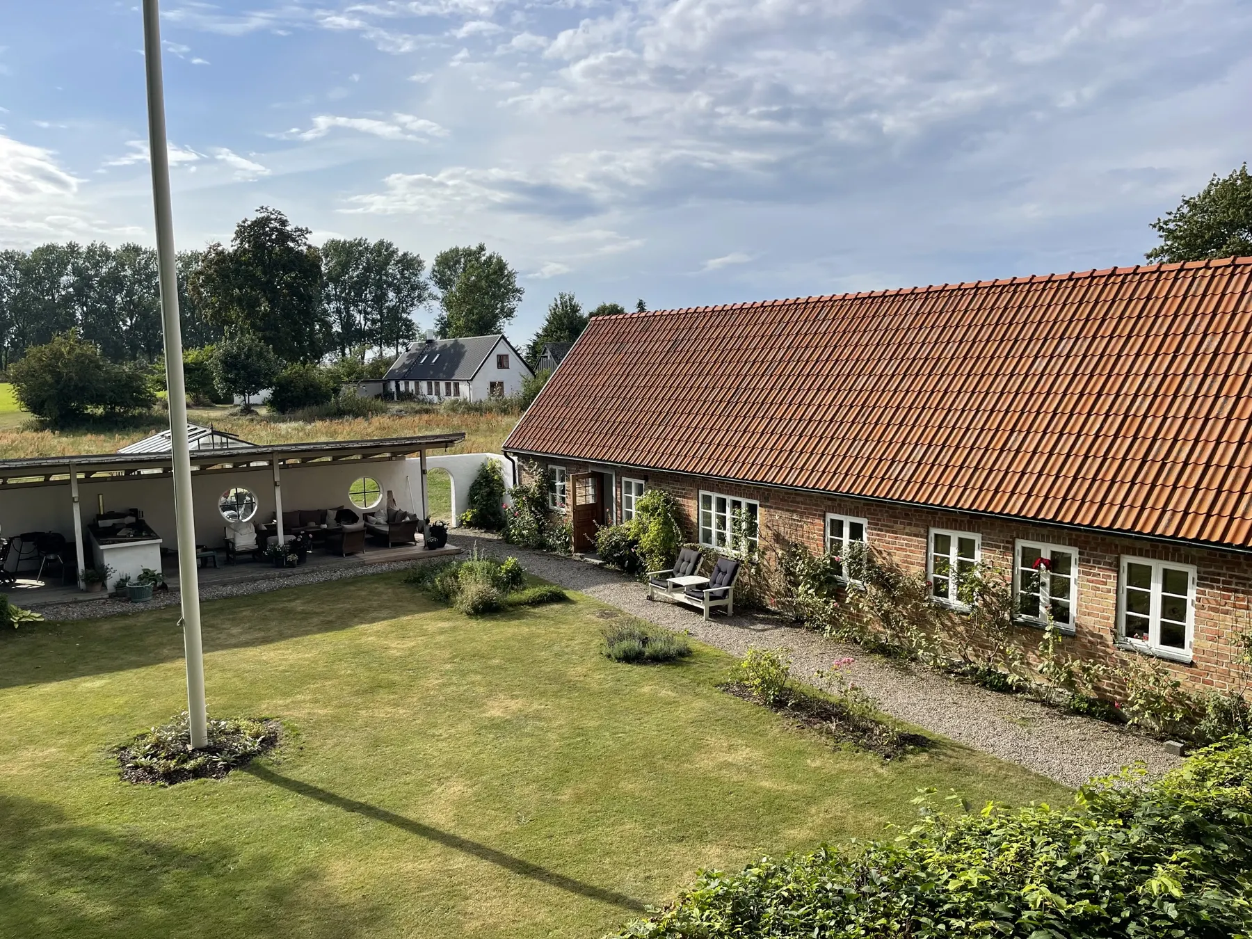 Trädgården med gräsmatta, flaggstång och en tegelbyggnad med rött tegeltak