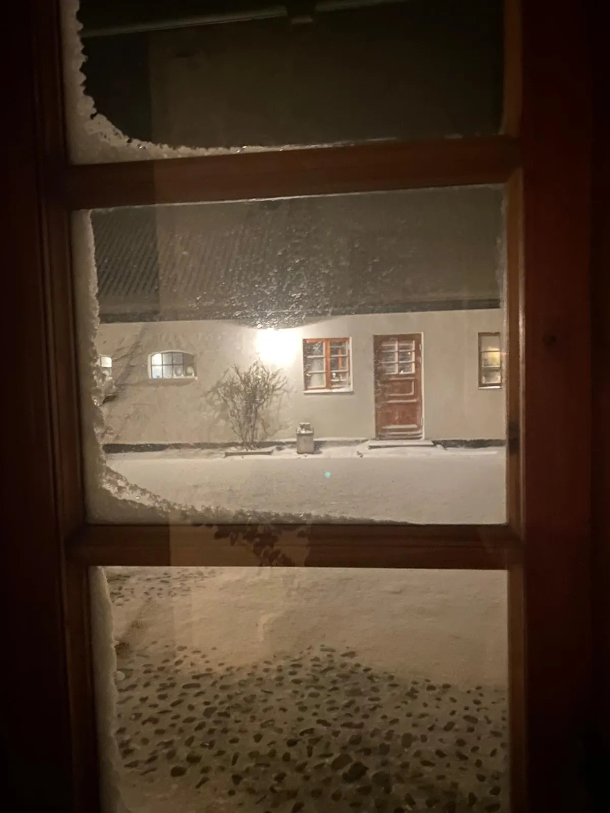 Utsikt genom ett frostigt fönster mot en upplyst vit länga i snön
